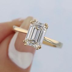 a close up of a person holding a ring with an emerald cut diamond in it