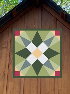 a quilt hanging on the side of a wooden building with trees in the back ground