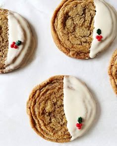 four cookies with white icing and red berries on them are arranged next to each other