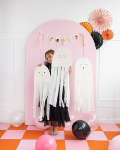 a woman standing in front of a pink wall holding up two white ghost shaped balloons