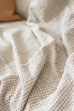 a white blanket sitting on top of a bed next to a brown pillow and pillows