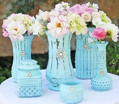 three blue vases filled with flowers sitting on top of a white table covered in doily