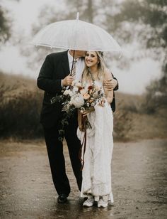 a bride and groom are walking under an umbrella in the rain, holding their bouquets