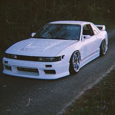 the white car is parked on the side of the road in front of some trees