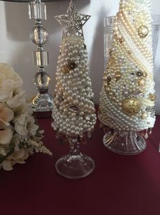 three christmas trees made out of pearls and other beads on a table next to flowers