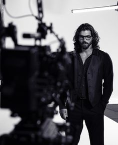 a man with long hair and glasses standing in front of a camera on a tripod