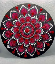 a red and white flower painted on a black plate with polka dots in the center