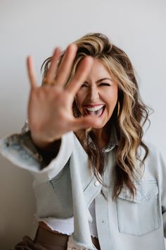 a woman is making the vulcan sign with her hand while smiling and wearing a white shirt