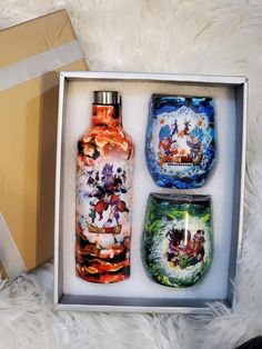 three colorful glass bottles in a box on a white furnishing area next to a gold gift box