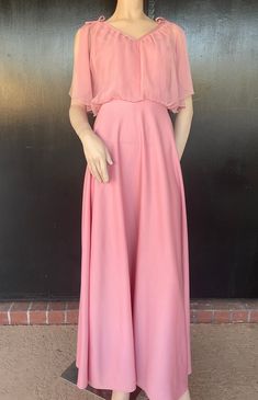 1970s maxi dress. Pink polyester. Polyester chiffon bodice overlay. Decorative bows on shoulders. Nylon zip back. Measurements 36" bust 26" waist 16" bodice length  58" length 44" hips Lovely dress shows well, with no obvious damage or wear. Pink Empire Waist Maxi Dress For Evening, Pink Empire Waist Maxi Dress For Bridesmaid, Pink Chiffon Maxi Dress For Prom Season, Pink Chiffon Evening Maxi Dress, Pink Flowy Maxi Dress For Prom, Flowy Pink Maxi Dress For Evening, Pink Full Length Maxi Dress For Spring, Vintage Pink Chiffon Dress, Pink Chiffon Cocktail Maxi Dress