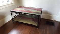 a multicolored table sitting on top of a hard wood floor next to a window