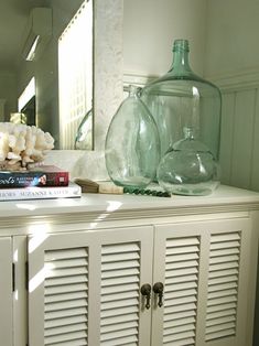 a white cabinet with books and vases on top of it next to a mirror