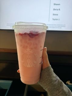 a person holding up a starbucks drink in front of a screen