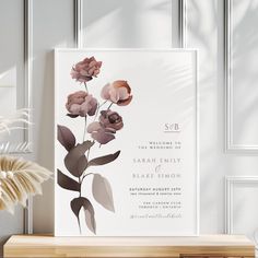 a wedding card with flowers on it sitting next to a vase and potted plant