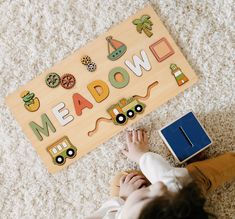 a baby laying on the floor next to a wooden board that says meadow with cars and trucks