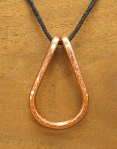 a copper pendant on a black cord is hanging from a wooden table with a brown leather cord