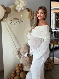 a woman in a white dress standing next to a teddy bear and balloon arch with the words baby expo written on it