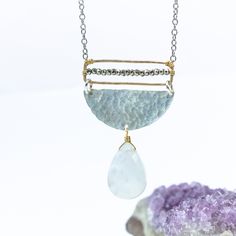 Embrace the enchanting allure of our Moonstone Radiance Necklace, a harmonious blend of celestial elegance and artistic craftsmanship. At its heart, a large moonstone, glowing with an ethereal light, gracefully hangs from a textured silver half circle, capturing the essence of lunar mystique. Above, a delicate gold rectangle, meticulously adorned with tiny sparkling pyrite gemstones, stretches the length of the disc, adding a touch of subtle brilliance to the design. The interplay of textures an Artisan Silver Necklace With Moon Phase Detail, Artisan Silver Necklace With Moon Phase, Artisan Silver Necklace With Moon Charm, Artisan Silver Jewelry With Moon Charm, Artisan Silver Jewelry With Moon Phase, Elegant Crescent Moonstone Necklace, Handmade Ethereal White Necklace, Handmade White Ethereal Necklace, Elegant Handmade Half Moon Necklace