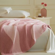 a bed covered in a pink blanket next to a night stand with flowers on it