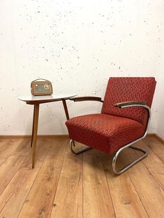 a red chair sitting next to a table on top of a hard wood floor