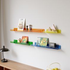 three shelves on the wall above a table with fruit and books in front of it