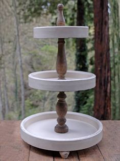 three tiered cake stand sitting on top of a wooden table in front of trees