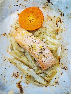 a piece of salmon and some vegetables on a white plate with an orange wedged in it