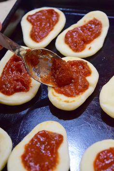 someone is spooning ketchup onto small pizzas