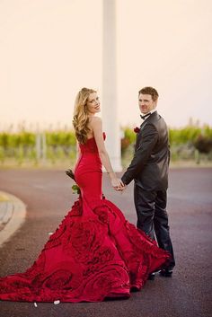 a man in a tuxedo and a woman in a red dress holding hands