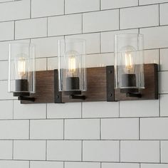 three light fixtures mounted on a white brick wall with wood and glass shades in an industrial style