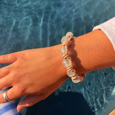 a woman's hand with two bracelets on her wrist next to a swimming pool