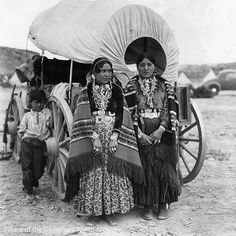 two women standing next to each other in front of a covered wagon