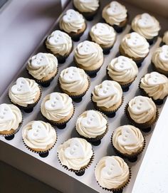 cupcakes with white frosting and buttons are in a box on the table