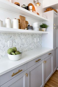 a bowl of broccoli is sitting on the counter in this white and gold kitchen