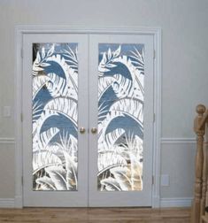 two glass doors with palm trees on them in front of a white wall and wooden stairs