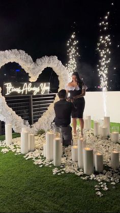 a man and woman standing in front of a heart - shaped sign surrounded by candles