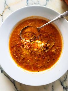 a white bowl filled with soup on top of a marble counter topped with a spoon