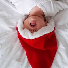 a baby in a santa suit laying on top of a white blanket with his nose sticking out