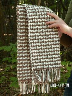 a woman is holding up a brown and white scarf in the woods with her hands