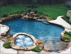 an outdoor swimming pool surrounded by rocks and water features a hot tub in the middle