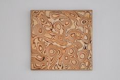 a wooden square with an abstract design on the surface, mounted on a wall in a white walled room