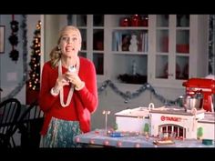 a woman standing in front of a table with a cake on it and a doll house behind her