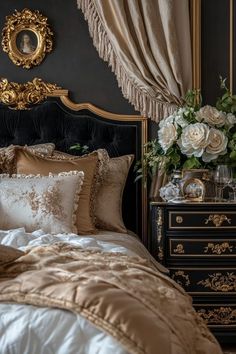 a bed with gold and white comforter next to a black dresser topped with flowers