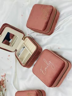 three pink jewelry cases sitting on top of a white bed next to each other with writing on them