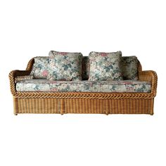 a wicker couch with floral cushions on it's back and sides, against a white background