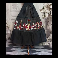 "Step into the fantastical world of Alice in Wonderland with this beautiful, handcrafted skirt featuring a stunning print inspired by Lewis Carroll's classic tale in vibrant black, red and gold.  The full skirt design adds a touch of whimsy and elegance, making it the perfect addition to any wardrobe.  Whether you're dressing up for a special occasion or adding a touch of Alice to your everyday look, this skirt is sure to make a statement. Order yours today and let the adventures begin!" Featuri Fantasy Skirt For Halloween Costume Party, Fitted Fantasy Skirt For Fantasy Events, Fitted Fantasy Skirt For Costume Party, Fantasy Costume Black Skirt, Fantasy Black Skirt For Costume, Black Costume Skirt With Attached Cancan, Black Skirt With Attached Cancan For Costume Party, Black Skirt With Attached Cancan For Costume, Fitted Fantasy Black Skirt