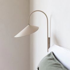 a white wall mounted lamp next to a bed with pillows on it and a green pillow