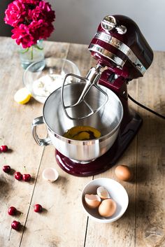 an electric mixer with eggs in it on a wooden table next to flowers and bowls