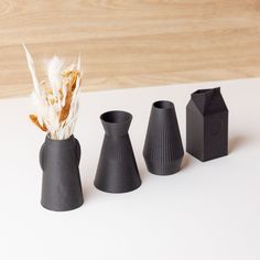 three black vases with feathers in them on a table