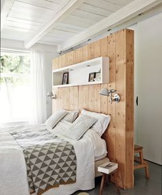 a bed with white sheets and pillows next to a wooden headboard in a bedroom